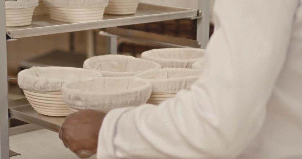 A close-up of empty bread proofing baskets lined with cloth, placed on a metal bakery rack. The baskets are ready for dough proofing in a professional bakery setting.